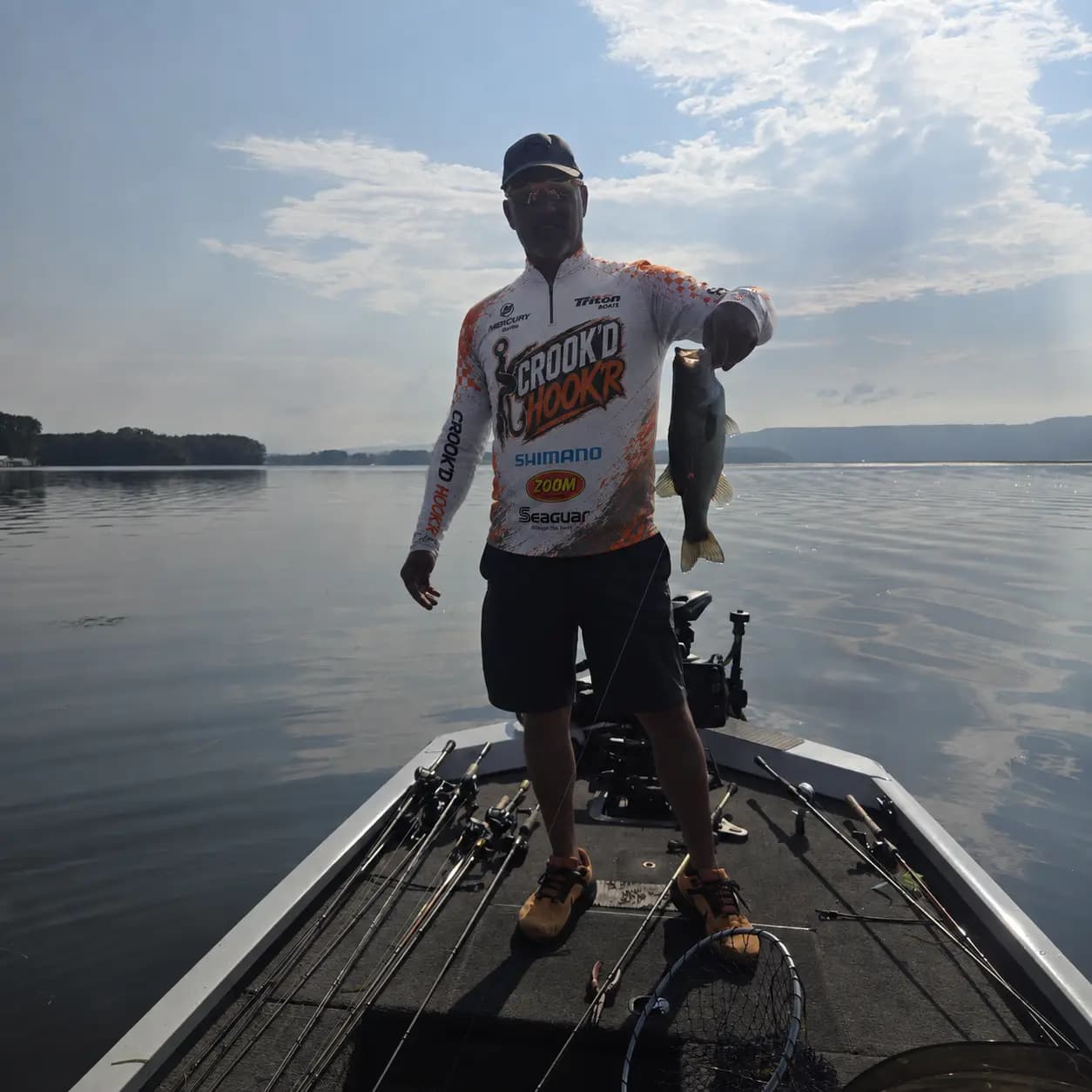 Matt holding a largemouth in a Crook’d Hook’r jersey in backlit morning conditions