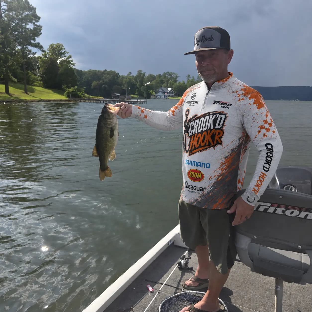 T holding a largemouth in a Crook’d Hook’r jersey near the Guntersville shoreline