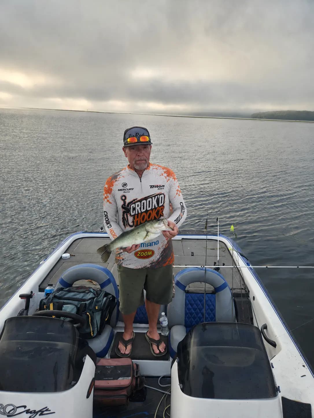 Mushy holding a largemouth on the boat in his Crook’d Hook’r jersey